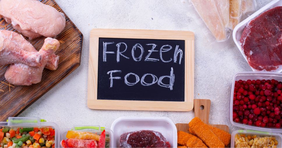 Lousa com a frase "Frozen Food" cercada por carnes e vegetais destaca a conservação de alimentos congelados.